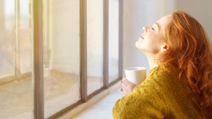 Young red-headed woman getting some sun from behind a window 